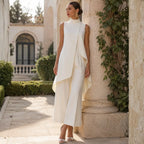 Ivory jumpsuit worn leaning against a stone pillar, showing the high neckline, draped front and wide cropped legs.