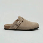 Side profile of a beige suede clog with adjustable buckle strap, cork-style footbed and black traction outsole.