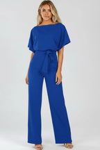 Model in a royal blue jumpsuit with draped sleeves, cinched waist tie and wide-leg pants paired with heels