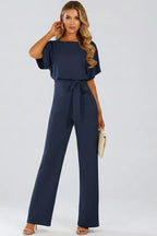 Navy blue jumpsuit with round neckline, batwing sleeves and wide-leg trousers, worn with a cream clutch
