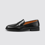 Side profile of a black leather-look penny loafer with classic saddle strap and stitched apron toe