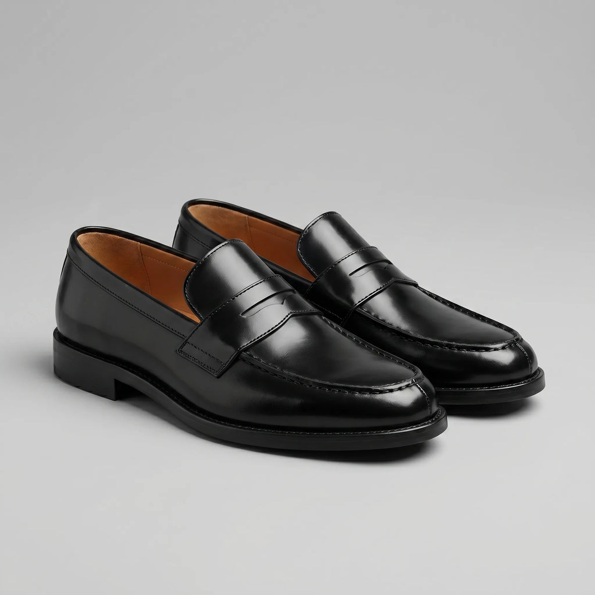 Angled pair view of black penny loafers showing glossy upper and tan leather-look lining
