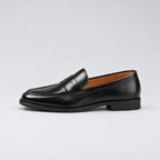 Clean side profile of the black penny loafer against a plain studio background