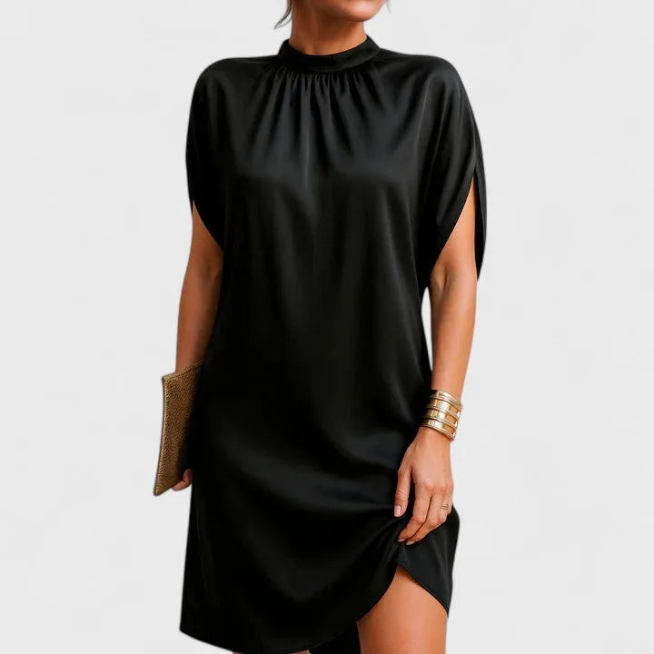 Woman modelling a black mock-neck shift dress with gathered collar and split cap sleeves, paired with a gold clutch