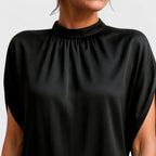 Detail shot of the gathered mock neckline and split short sleeve seam on the black satin-finish dress