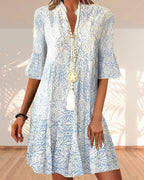 Close-up front view of a woman wearing a blue and white paisley print midi dress with a beaded tassel necklace