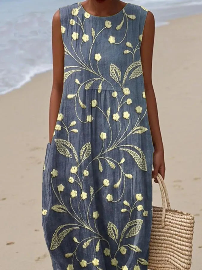Close-up view of the yellow floral embroidery and relaxed silhouette of the blue sleeveless midi dress.
