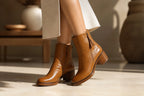 Close-up of a woman walking in camel leather ankle boots paired with a cream knit midi skirt