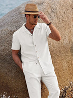 Close-up of man wearing white camp collar shirt with chest pocket, leaning against a rock, wearing a straw hat and sunglasses.