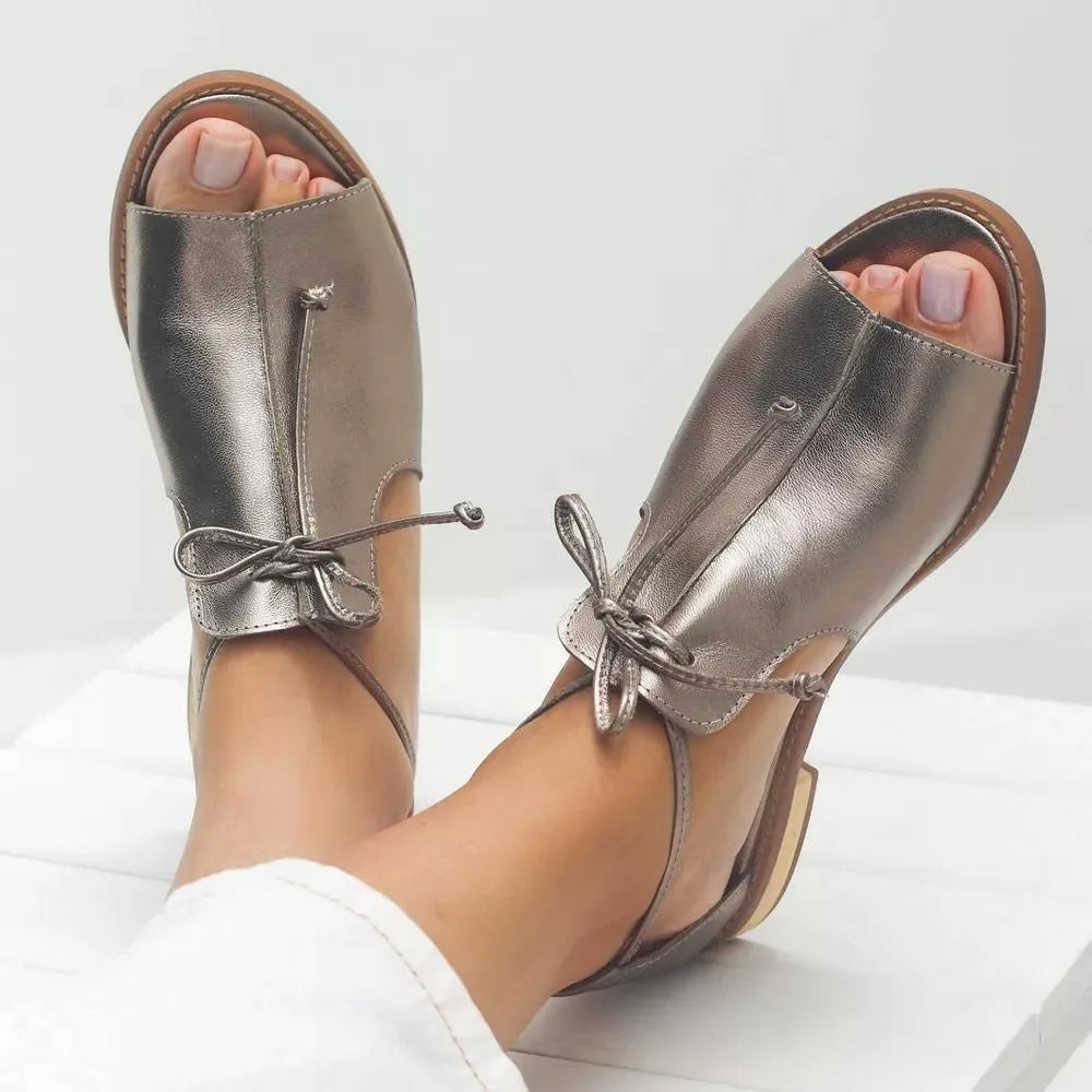 Side view of champagne metallic leather sandals with open toe, lace-up bow ankle strap and tan rubber sole