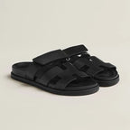 Black leather slide sandals with wide adjustable strap and cut-out panel detail on a black sole.