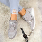 Overhead view of grey and silver sneakers on a sheepskin rug beside a watch and sunglasses