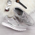 Close-up of beige and champagne metallic sneakers with one shoe held to show the ridged sole
