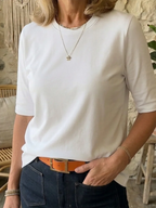 Close-up of a woman wearing a white half-sleeve crew neck t-shirt with layered gold necklaces and jeans