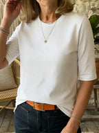 Side angle of the white half-sleeve cotton t-shirt paired with a gold chain necklace, hand raised to hair