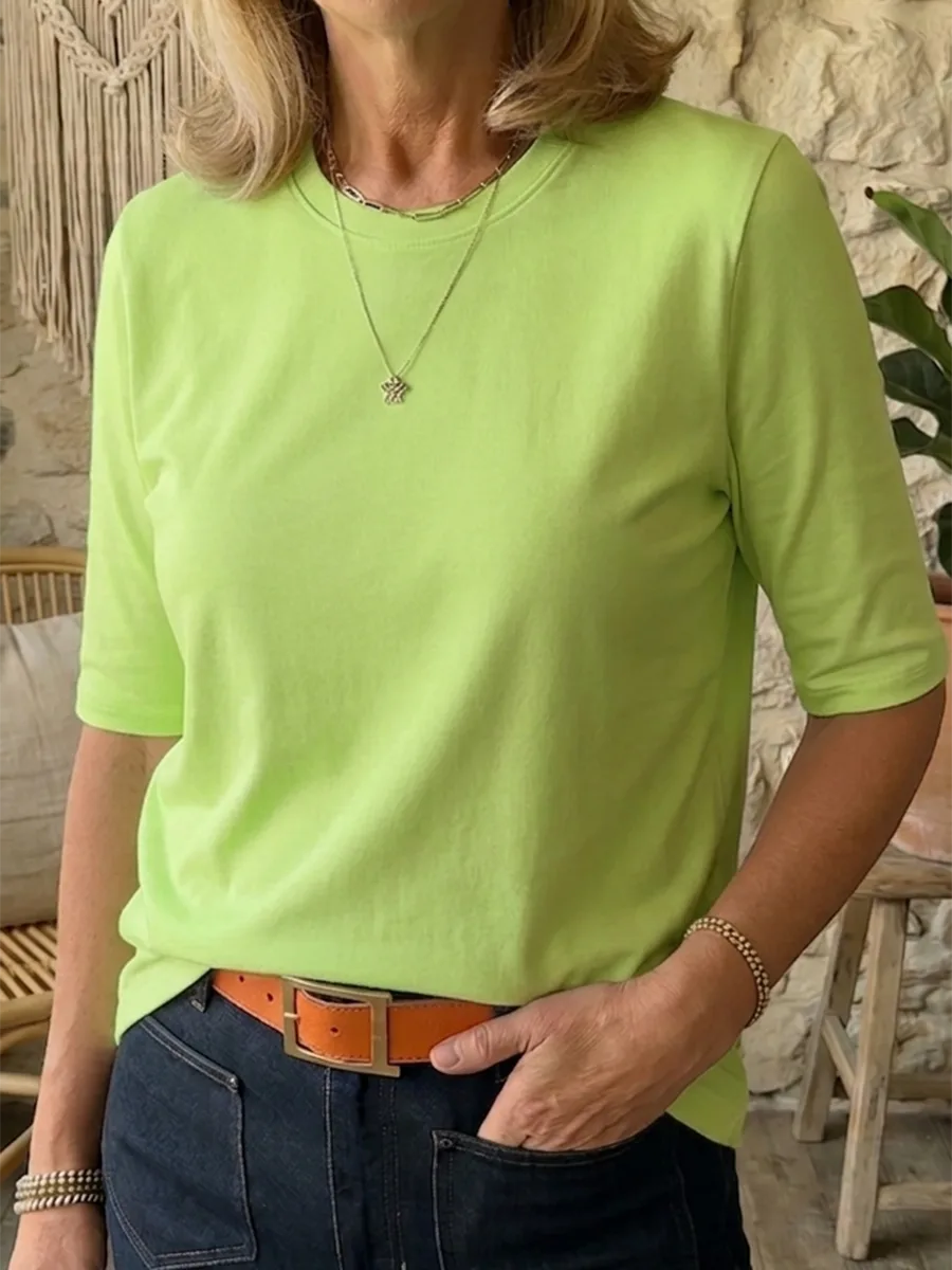 Bright lime green half-sleeve t-shirt worn with a layered necklace and dark jeans, close front view