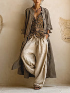 Woman wearing a long grey linen duster coat over a printed sleeveless top and beige wide-leg linen pants, hand in pocket