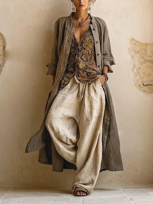Woman wearing a long grey linen duster coat over a printed sleeveless top and beige wide-leg linen pants, hand in pocket