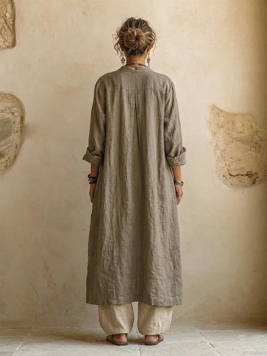 Back view of the long grey linen duster coat with centre box pleat, worn over the beige wide-leg linen pants