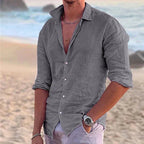 Grey cotton linen shirt styled casually open at the top, worn on sand with ocean waves in the background