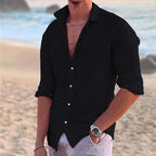 Black button-down linen shirt with rolled sleeves, worn untucked over light trousers on a beach