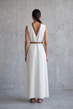 Back view of the cream linen V-neck maxi dress showing the tan leather neckline trim and belt tied at the waist