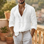 Man wearing a white button-up cotton linen shirt, untucked, styled with light trousers and layered gold necklaces.