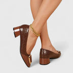 Back view of brown croc-embossed block heel pumps with gold buckle detail, paired with a gold ankle chain