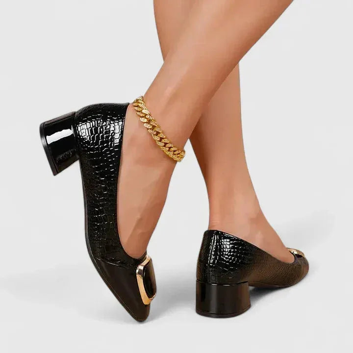 Angled rear view of black croc-textured block heel pumps with a glossy patent toe and gold buckle accent