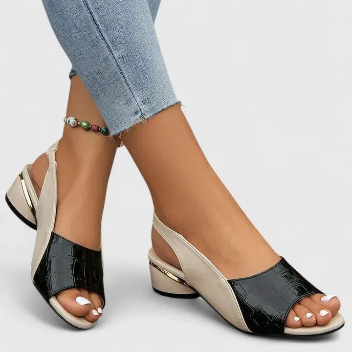 Side view of black croc-embossed leather slingback sandals with beige panel and gold-trimmed block heel, worn with cropped jeans.
