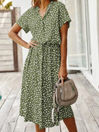 Model holding a brown bag, wearing an olive green midi shirt dress with a white dot print and collar