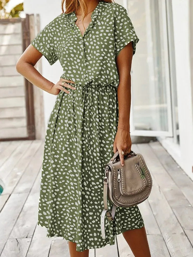 Model holding a brown bag, wearing an olive green midi shirt dress with a white dot print and collar