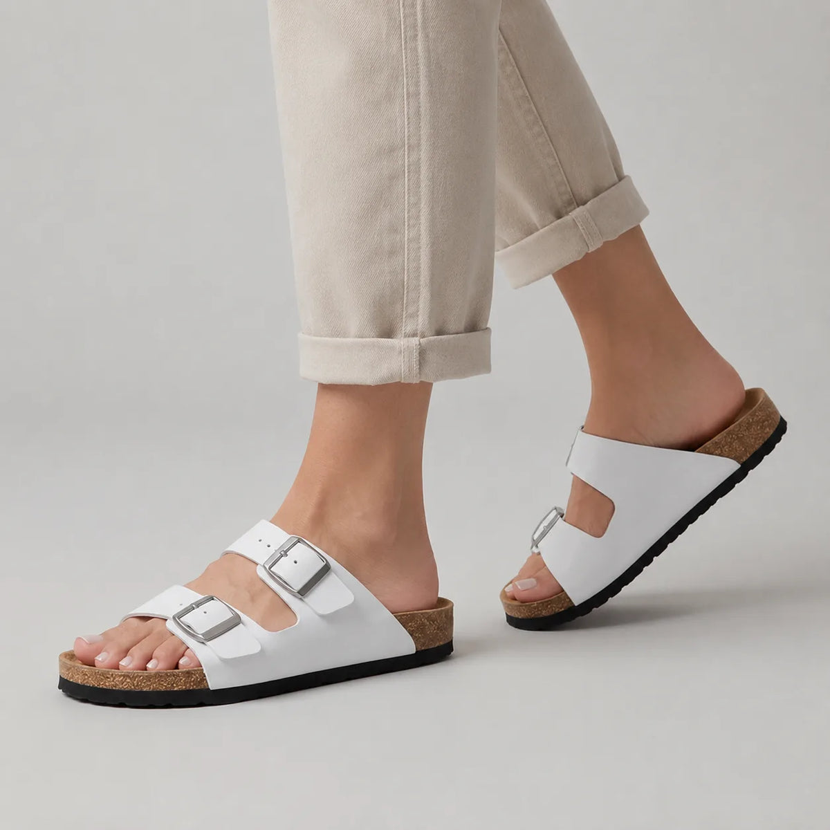 White double-strap buckle sandal worn on foot, paired with rolled-up beige jeans, showing cork footbed and side profile