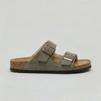 Side view of a khaki green suede double-strap sandal with bronze buckles and cork sole