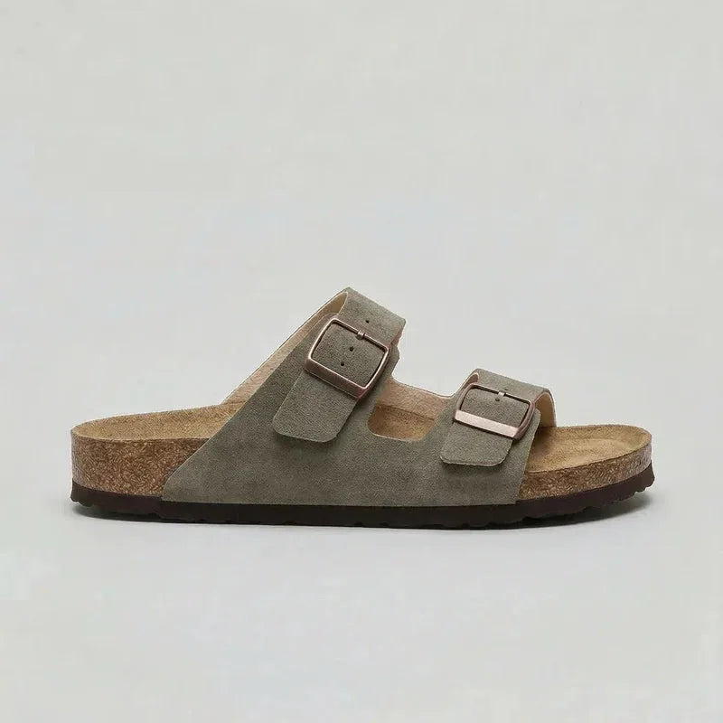 Side view of a khaki green suede double-strap sandal with bronze buckles and cork sole
