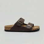 Side view of a brown double-strap buckle sandal with gold-tone buckles and tan cork footbed