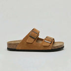 Side view of a tan brown suede double-strap sandal with bronze buckles and cork footbed