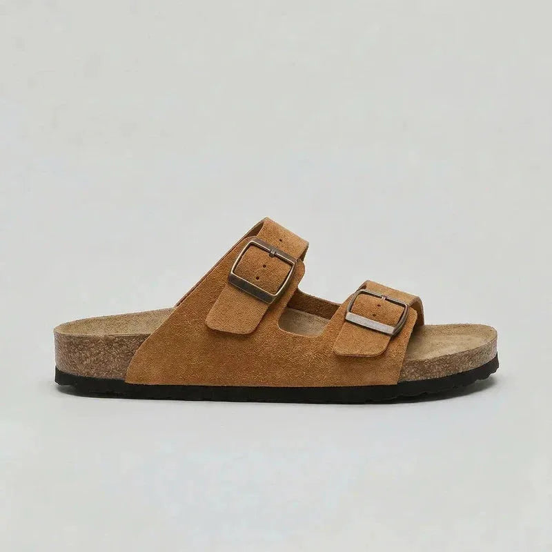 Side view of a tan brown suede double-strap sandal with bronze buckles and cork footbed