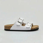 Side view of a white double-strap buckle sandal with silver-tone buckles and natural cork sole