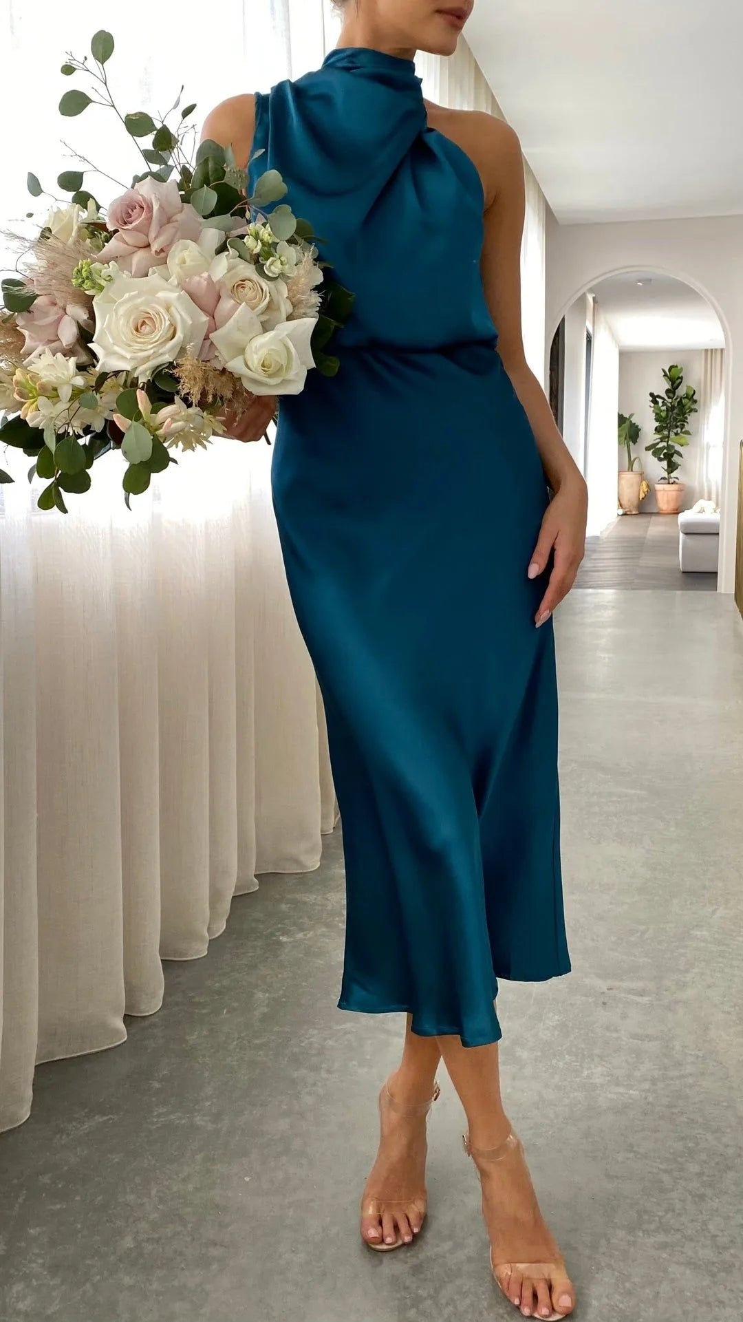 Close-up side view of teal satin dress with asymmetric draped collar, model holding floral bouquet