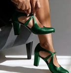 Close-up of emerald green leather strap heels showing the T-strap buckle detail and sturdy block heel.
