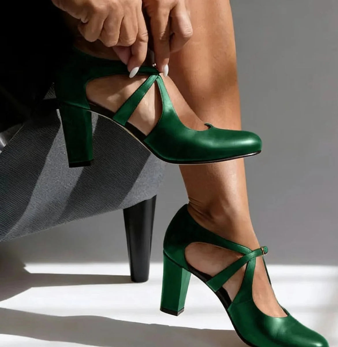 Close-up of emerald green leather strap heels showing the T-strap buckle detail and sturdy block heel.
