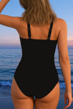 Back view of a plain black one-piece swimsuit with adjustable shoulder straps, worn at the beach
