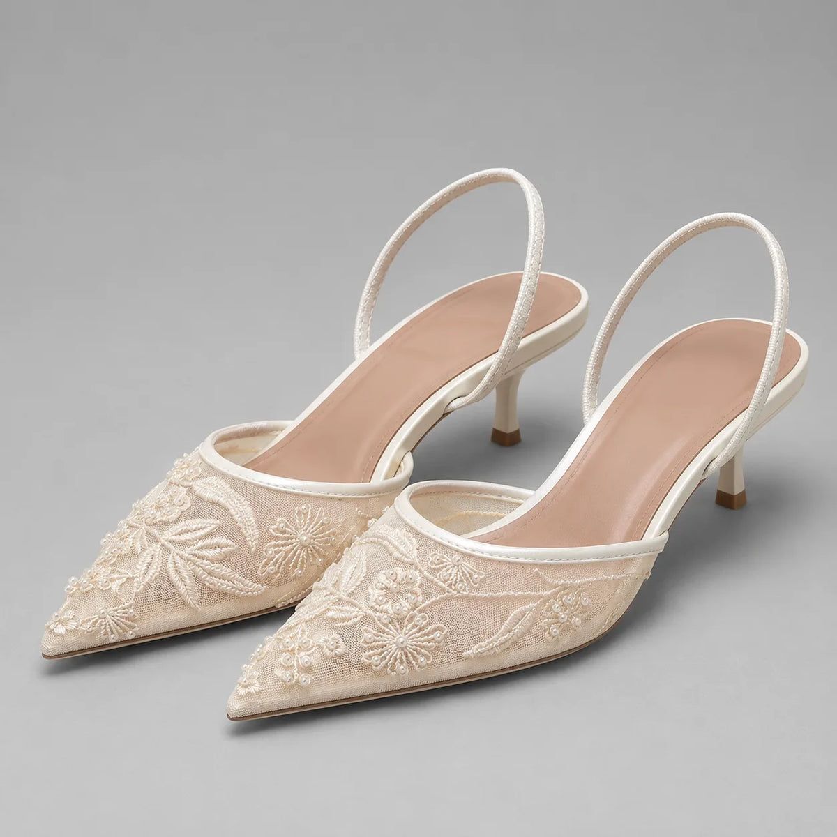 White embroidered mesh slingback heels with pointed toe, floral embroidery and slim kitten heel, side angle view.