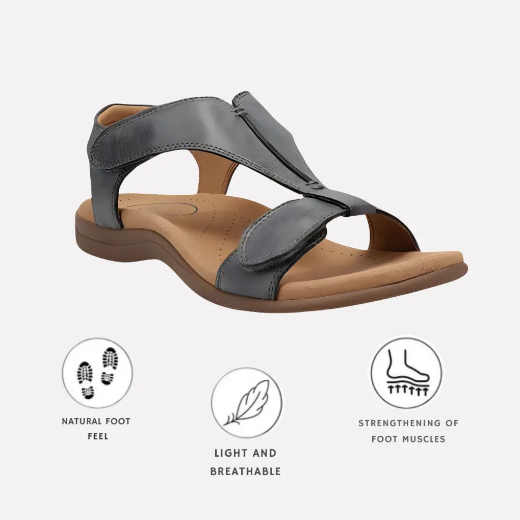 Grey leather T-strap sandal with cushioned tan footbed and brown sole, shown from an angle