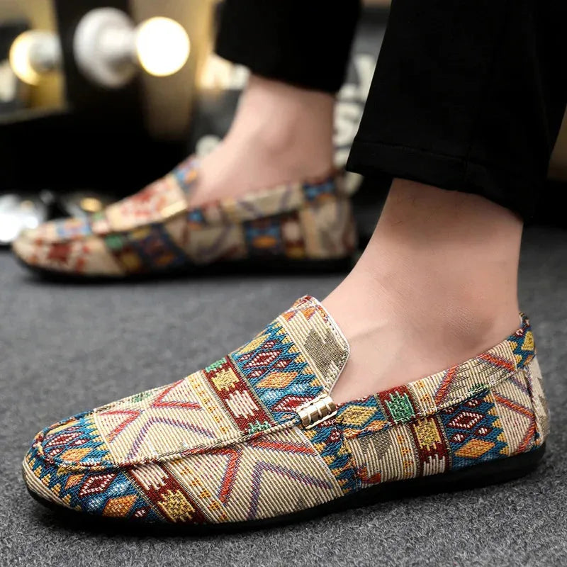 Close-up of a man's foot wearing a beige woven loafer with colourful geometric pattern and black trousers