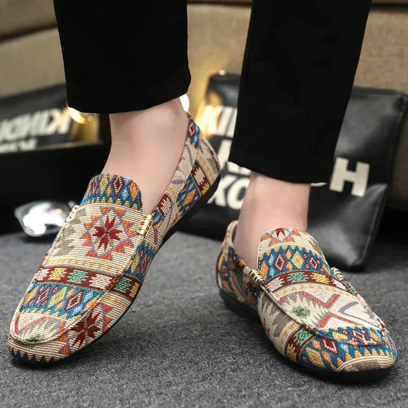 Side angle of a worn beige patterned loafer on foot, highlighting the gold saddle detail and slip-on fit