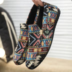 Hand holding a pair of black ethnic-pattern woven loafers, showing gold hardware and padded collar from above