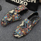 Top-down view of black patterned loafers with gold buckle detail placed on a grey textured surface