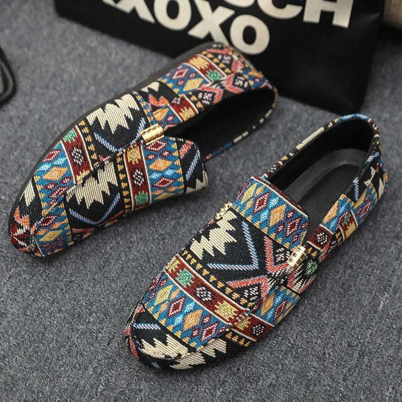 Top-down view of black patterned loafers with gold buckle detail placed on a grey textured surface